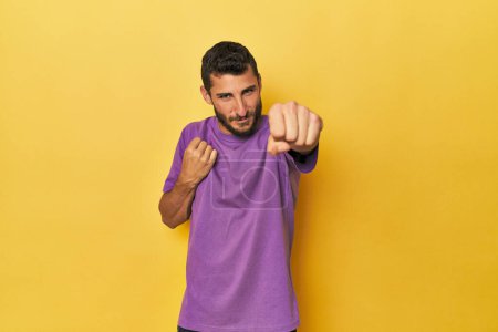 Téléchargez les photos : Jeune homme hispanique sur fond jaune jetant un coup de poing, colère, combats à cause d'une dispute, boxe. - en image libre de droit