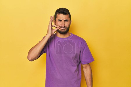Téléchargez les photos : Jeune homme hispanique sur fond jaune avec les doigts sur les lèvres gardant un secret. - en image libre de droit