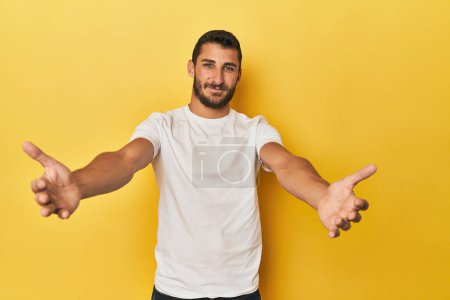 Téléchargez les photos : Jeune homme hispanique sur fond jaune montrant une expression bienvenue. - en image libre de droit