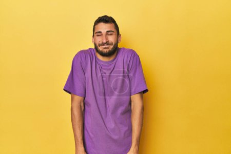 Téléchargez les photos : Jeune homme hispanique sur fond jaune rit et ferme les yeux, se sent détendu et heureux. - en image libre de droit