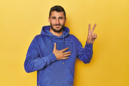 Photo for Young Hispanic man on yellow background taking an oath, putting hand on chest. - Royalty Free Image