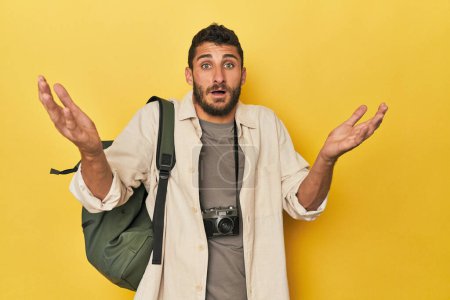 Téléchargez les photos : Jeune photographe de voyage hispanique pose recevoir une agréable surprise, excité et lever la main. - en image libre de droit