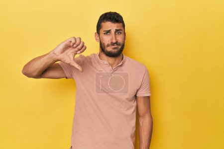 Téléchargez les photos : Jeune homme hispanique sur fond jaune montrant un geste détestable, les pouces baissés. Concept de désaccord. - en image libre de droit
