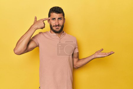 Photo for Young Hispanic man on yellow background holding and showing a product on hand. - Royalty Free Image