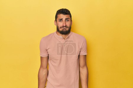 Photo for Young Hispanic man on yellow background shrugs shoulders and open eyes confused. - Royalty Free Image