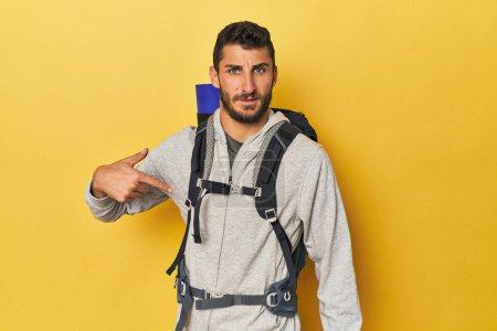 Téléchargez les photos : Jeune homme hispanique prêt pour la randonnée personne pointant à la main vers un espace de copie chemise, fier et confiant - en image libre de droit