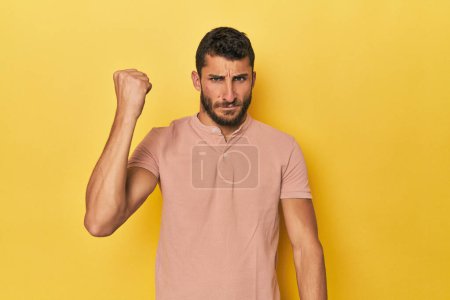 Photo for Young Hispanic man on yellow background showing fist to camera, aggressive facial expression. - Royalty Free Image