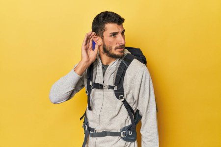 Téléchargez les photos : Jeune homme hispanique prêt pour la randonnée en essayant d'écouter un potins. - en image libre de droit