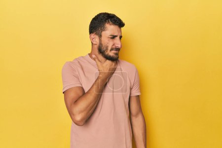 Foto de Hombre joven hispano de fondo amarillo sufre dolor de garganta debido a un virus o infección. - Imagen libre de derechos
