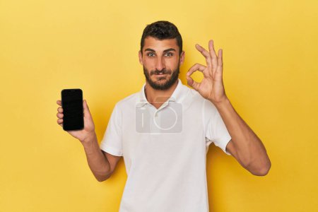 Téléchargez les photos : Jeune homme hispanique montre écran de téléphone joyeux et confiant montrant geste ok. - en image libre de droit