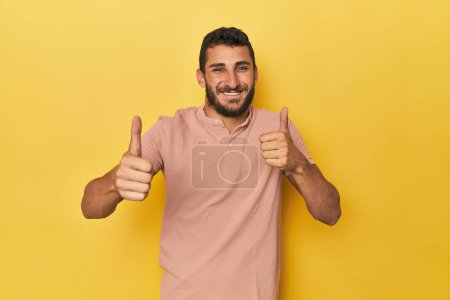 Téléchargez les photos : Jeune homme hispanique sur fond jaune levant les pouces vers le haut, souriant et confiant. - en image libre de droit