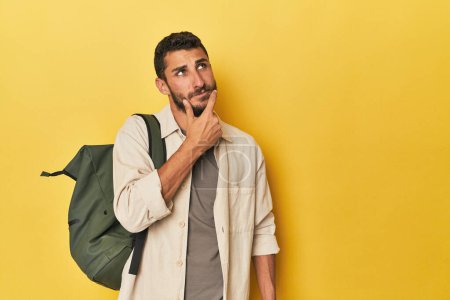 Foto de Joven hispano con mochila de viaje mirando de lado con expresión dudosa y escéptica. - Imagen libre de derechos