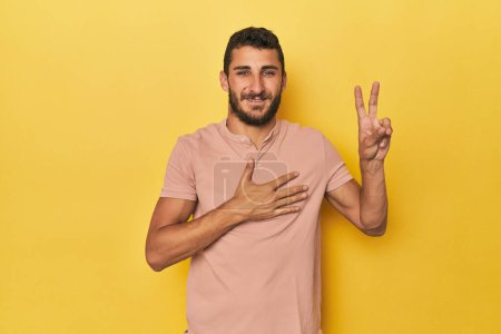 Téléchargez les photos : Jeune homme hispanique sur fond jaune prêtant serment, mettant la main sur la poitrine. - en image libre de droit