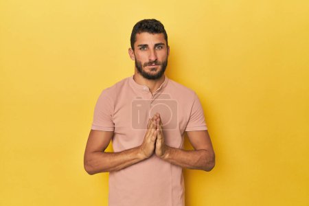 Photo for Young Hispanic man on yellow background praying, showing devotion, religious person looking for divine inspiration. - Royalty Free Image