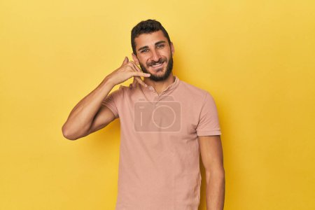 Foto de Joven hispano sobre fondo amarillo mostrando un gesto de llamada telefónica móvil con los dedos. - Imagen libre de derechos