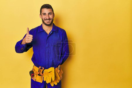 Photo for Young Hispanic man in a blue jumpsuit Young Hispanic man in a blue jumpsuitsmiling and raising thumb up - Royalty Free Image