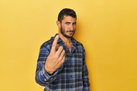 Téléchargez les photos : Jeune homme hispanique sur fond jaune pointant du doigt vers vous comme s'il vous invitait à vous rapprocher. - en image libre de droit