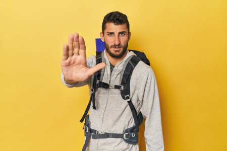 Photo for Young Hispanic man ready for hiking standing with outstretched hand showing stop sign, preventing you. - Royalty Free Image