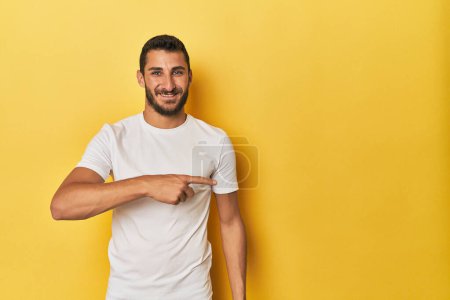 Photo for Young Hispanic man on yellow background smiling and pointing aside, showing something at blank space. - Royalty Free Image