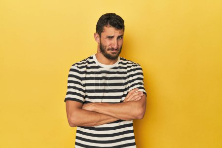 Photo for Young Hispanic man on yellow background frowning face in displeasure, keeps arms folded. - Royalty Free Image