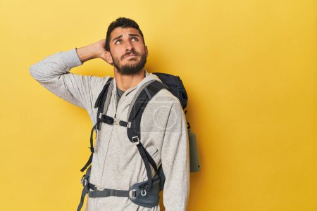 Téléchargez les photos : Jeune homme hispanique prêt pour la randonnée toucher l'arrière de la tête, penser et faire un choix. - en image libre de droit