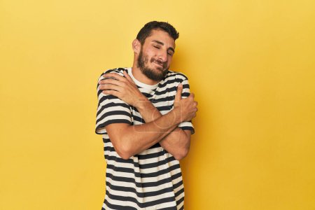 Foto de Joven hispano sobre un fondo amarillo abrazos, sonriente despreocupado y feliz. - Imagen libre de derechos