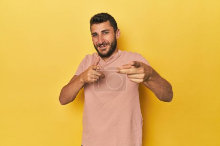 Téléchargez les photos : Jeune homme hispanique sur fond jaune pointant vers l'avant avec les doigts. - en image libre de droit