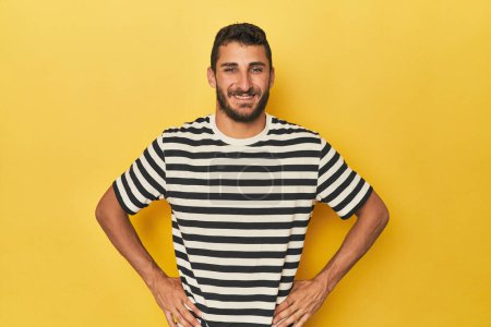 Téléchargez les photos : Jeune homme hispanique sur fond jaune confiant garder les mains sur les hanches. - en image libre de droit