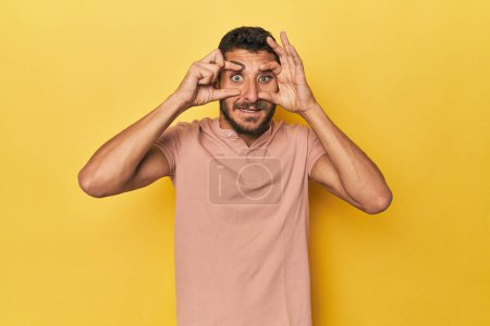 Téléchargez les photos : Jeune homme hispanique sur fond jaune gardant les yeux ouverts pour trouver une opportunité de succès. - en image libre de droit