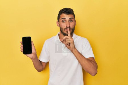 Téléchargez les photos : Jeune homme hispanique montre écran de téléphone garder un secret ou demander le silence. - en image libre de droit