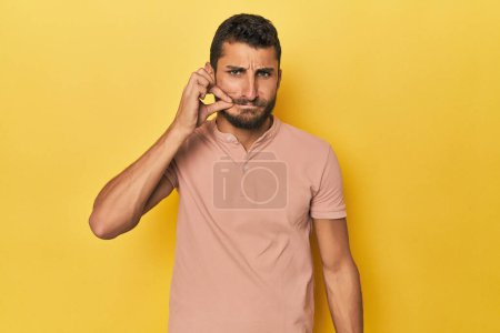 Photo for Young Hispanic man on yellow background with fingers on lips keeping a secret. - Royalty Free Image