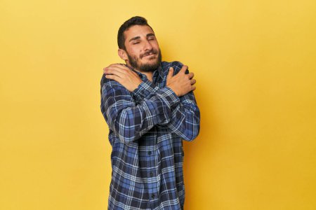 Téléchargez les photos : Jeune homme hispanique sur fond jaune câlins, souriant insouciant et heureux. - en image libre de droit
