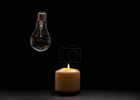Brennende Kerze in der Nähe einer ausgeschalteten Glühbirne im dunklen Haus. Stromausfall, Stromausfall, Energiekrise oder Stromausfall, Konzeptbild.