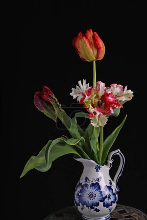 Parrot tulips in placed in a flowerpot on a table with a sleek black background, creating a striking contrast with the colorful petals