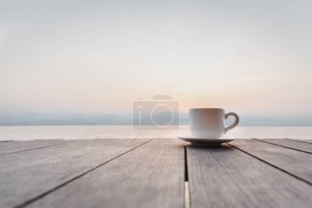 Photo for Cup of coffee on wooden deck over sunrise with river mountain in background - Royalty Free Image