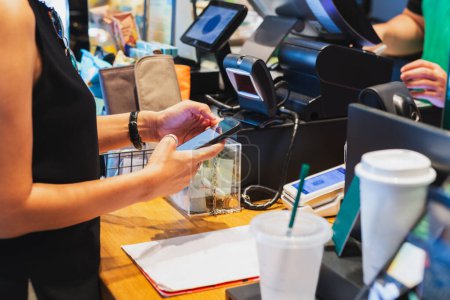 Téléchargez les photos : Femme numérisation QR code paiement via téléphone mobile à la caisse dans le café - en image libre de droit