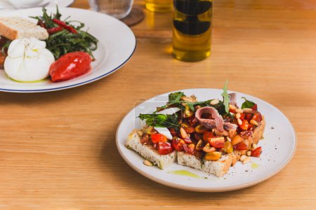 Photo for Appetizer bruschetta topped with tomatoes wild rocket leavesand anchovy - Royalty Free Image