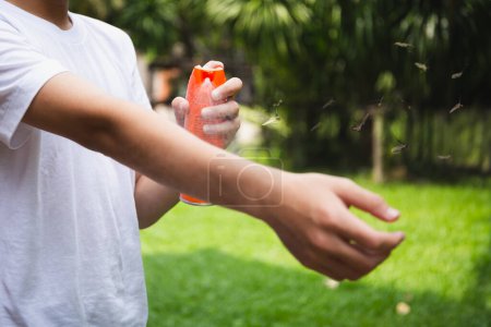 Junge sprüht mit Mückenflug Insektenschutzmittel auf Haut im Garten