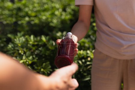 Téléchargez les photos : Main de femme donnant une bouteille en verre de boisson de jus nutritive avec fond de feuille de plante - en image libre de droit