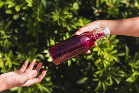 Téléchargez les photos : Main de femme donnant une bouteille en verre de boisson de jus nutritive avec fond de feuille de plante - en image libre de droit