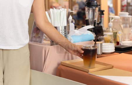 Woman taking iced coffee in a take away cup from cafe counter