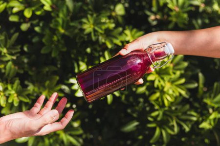 Téléchargez les photos : Femme main donnant une bouteille en verre de boisson de jus nutritive avec fond de feuille de plante - en image libre de droit