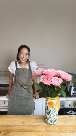 Téléchargez les photos : Femme heureuse dans tablier à la chambre avec fleur - en image libre de droit