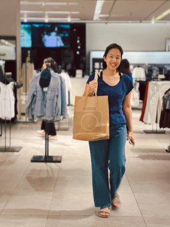 Téléchargez les photos : Femme heureuse faisant des achats de vêtements et tenant le sac en papier produit - en image libre de droit