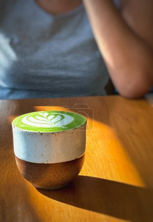 Téléchargez les photos : Tasse de thé vert matcha latte sur table en bois avec femme en arrière-plan - en image libre de droit