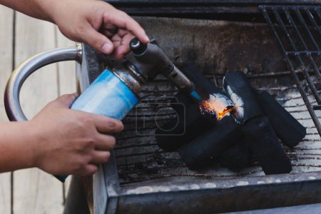 Mann zündet mit Grillfackel Feuer für Holzkohle