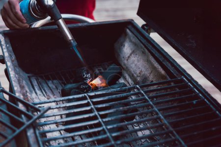 Man using BBQ lighter torch to start fire for charcoal