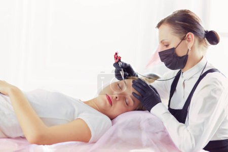 Téléchargez les photos : Jeune femme subissant une procédure de maquillage permanent des sourcils dans un salon de beauté. - en image libre de droit