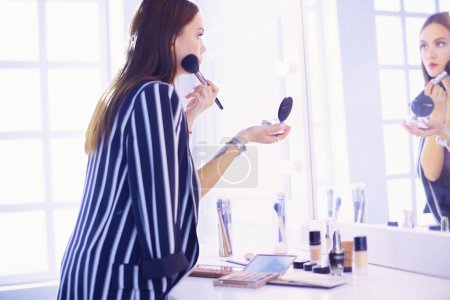 Foto de Hermosa chica mirando en el espejo y la aplicación de cosméticos con un cepillo grande. - Imagen libre de derechos