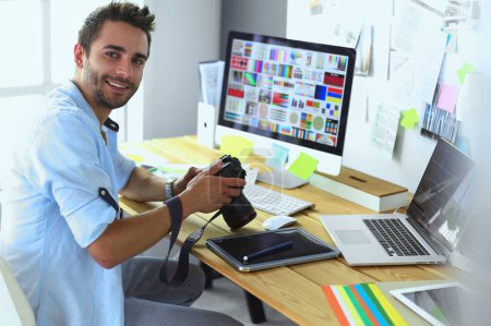 Foto de Retrato del joven diseñador sentado en el estudio gráfico frente a la computadora portátil y el ordenador mientras trabaja en línea - Imagen libre de derechos